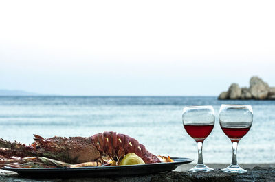 Close-up of lobster and drink on table by sea against clear sky