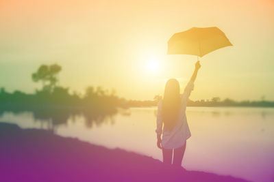 Rear view of woman standing by lake against sky during sunset