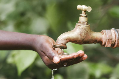 Close-up of hand holding faucet against blurred background