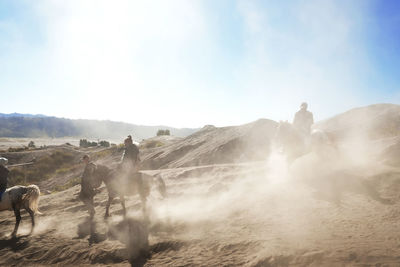 People riding horses on sand against sky