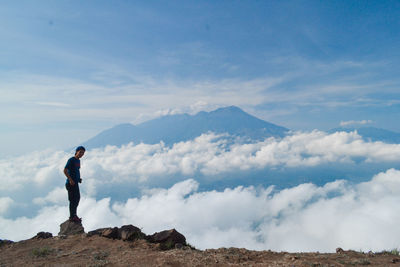 Side view of man standing on rock against sky