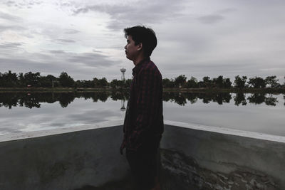 Side view of young man looking at lake against sky