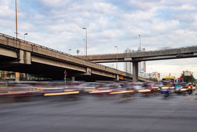 Cars on bridge over road against cloudy sky