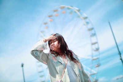 Low angle view of woman standing against sky with ferris wheel in background