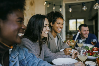 Happy female and male friends sitting together at dining table in patio