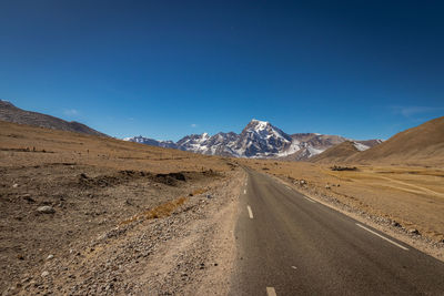 Road leading towards mountains against blue sky