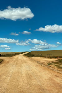 Dirt road amidst field against blue sky