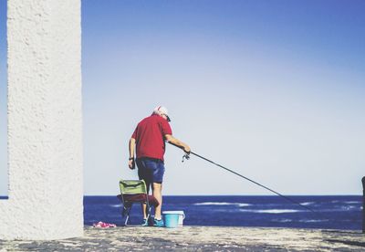 Rear view of man fishing in sea against clear sky