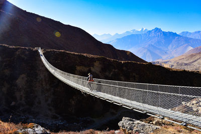 Man walking on footbridge against mountain