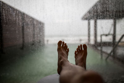 Low section of person relaxing against window during rainy season