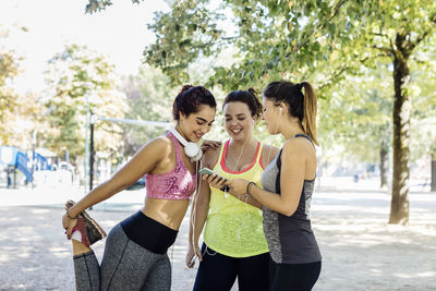 Smiling young female friends in sports clothing using smart phone at park