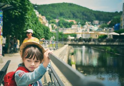 Girl looking away by railing over river against sky