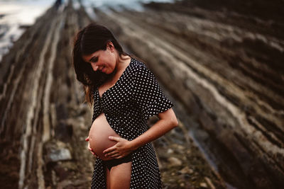 Side view thoughtful pregnant woman standing on rough rock near sea in nature