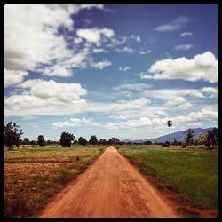 Road passing through field against cloudy sky