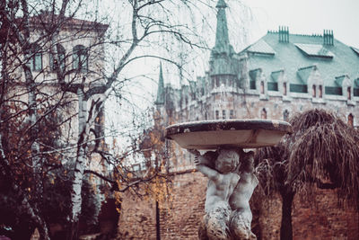 Statue by bare trees in city during winter