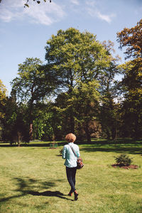 Full length of woman walking on grassy field against trees at forest