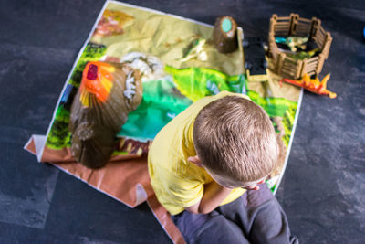 High angle view of cute boy sitting by toy on carpet at home