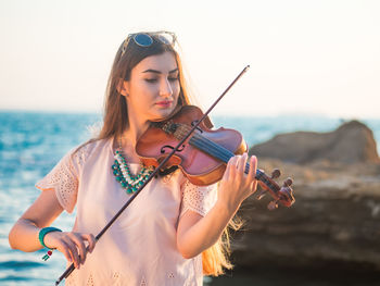 Young woman playing violin while by sea