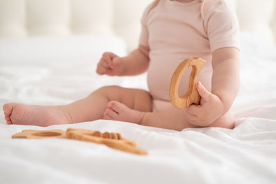 Baby girl in light pink bodysuit playing with wooden toys on white bedding on bed