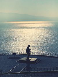 Silhouette man standing by sea against sky during sunset