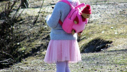 Midsection of girl carrying pink bag while standing on field