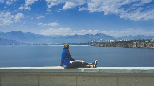 Woman sitting on retaining wall at sea against sky