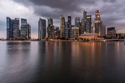 Illuminated buildings by river against sky in city