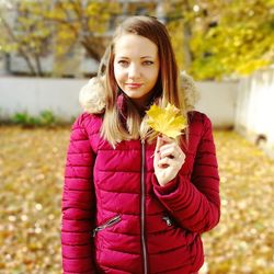 Portrait of beautiful young woman holding dry leaf standing in yard