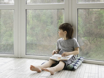 Kid sits on floor and reads book. intellectual leisure for children while it's raining outside.