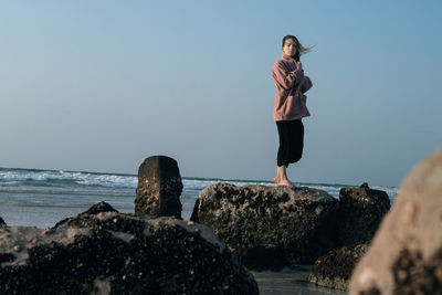 Woman standing on rock by sea against clear sky