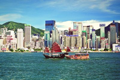 Boats sailing in sea by cityscape against sky