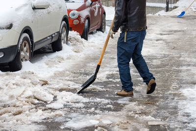 A man removes snow and ice from the sidewalk with a shovel on a winter day.