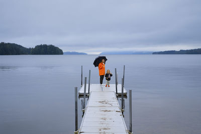 Rear view of man standing on pier over lake