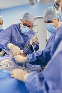 Mature doctor operating shoulder arthroscopic surgery with colleague while standing in operating room during covid-19