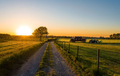 Dirt road amidst field against sky during sunset