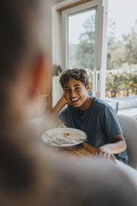 Happy multiracial boy leaning on elbow while sitting after having lunch at dining table