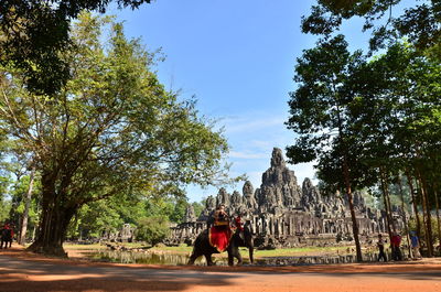 People riding on elephant outside bayon temple against sky