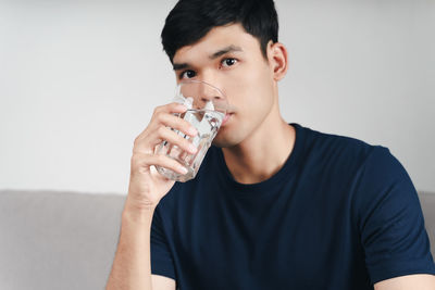 Portrait of young man drinking glass against white background