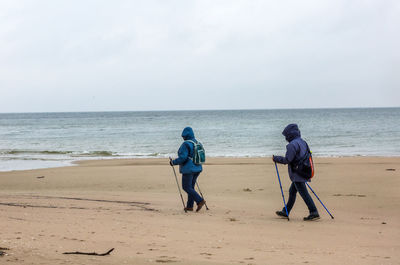 People with walking poles at beach against sky