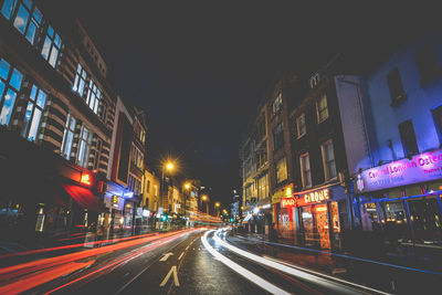 Light trails on road amidst buildings in city at night