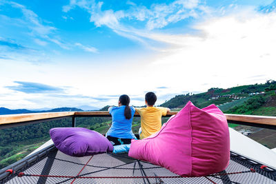 Rear view of friends sitting on pink water against sky