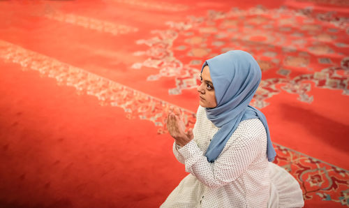 Woman looking away while standing against red wall