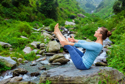 Side view of woman sitting on rock in forest