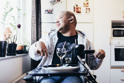 Happy disabled musician with drink sitting by window at recording studio