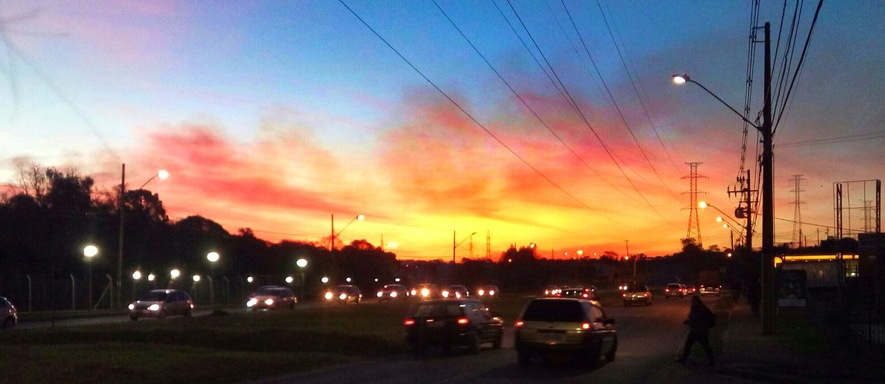 transportation, sunset, mode of transport, car, sky, silhouette, land vehicle, illuminated, street light, cloud - sky, dusk, electricity pylon, road, street, dramatic sky, orange color, power line, outdoors, cloud, lighting equipment