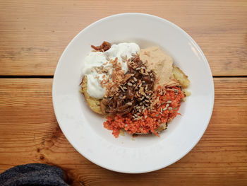 Directly above shot of hummus with baked potatoes served in plate on wooden table