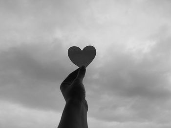 Silhouette hands holding heart against clouds