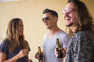 Cheerful friends having beer while standing against wall