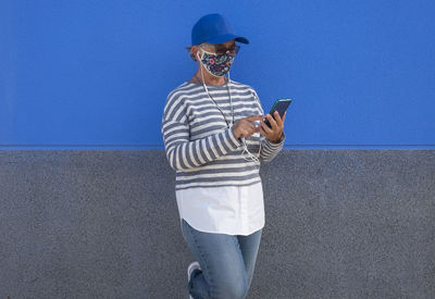 Senior woman wearing flu mask using phone against wall