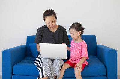 Full length of mother and daughter sitting on sofa